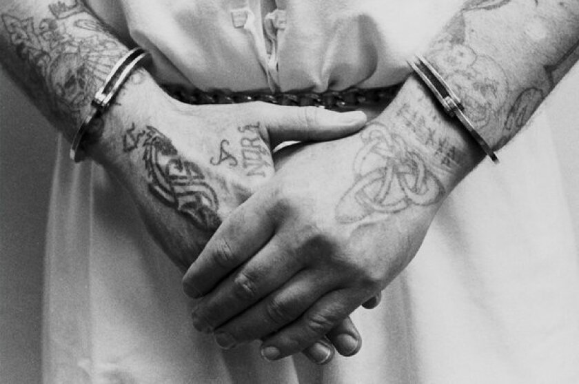 An inmate at Pelican Bay prison in Crescent City, Ca., shows his tattoos and handcuffs. In Germany, economists tried the classic prisoner's dilemma game on real prisoners -- and found them more likely to cooperate with each other than students.