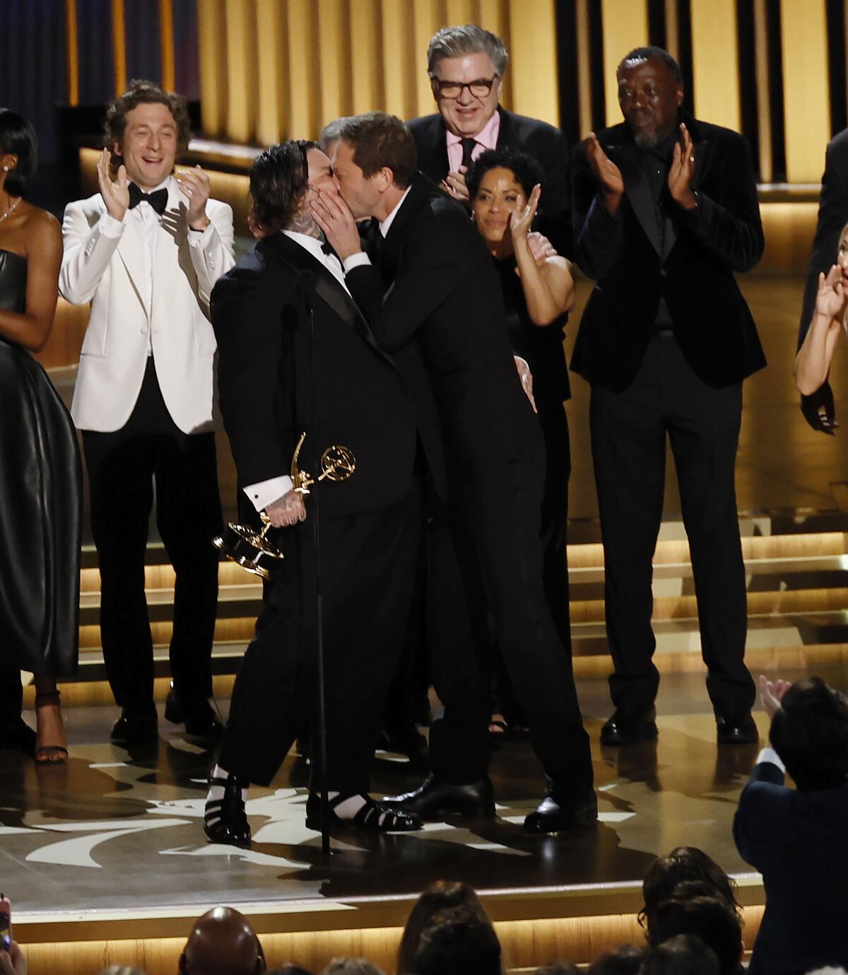 Matty Matheson and Ebon Moss-Bachrach kiss on stage while accepting "The Bear's" Emmy Award.