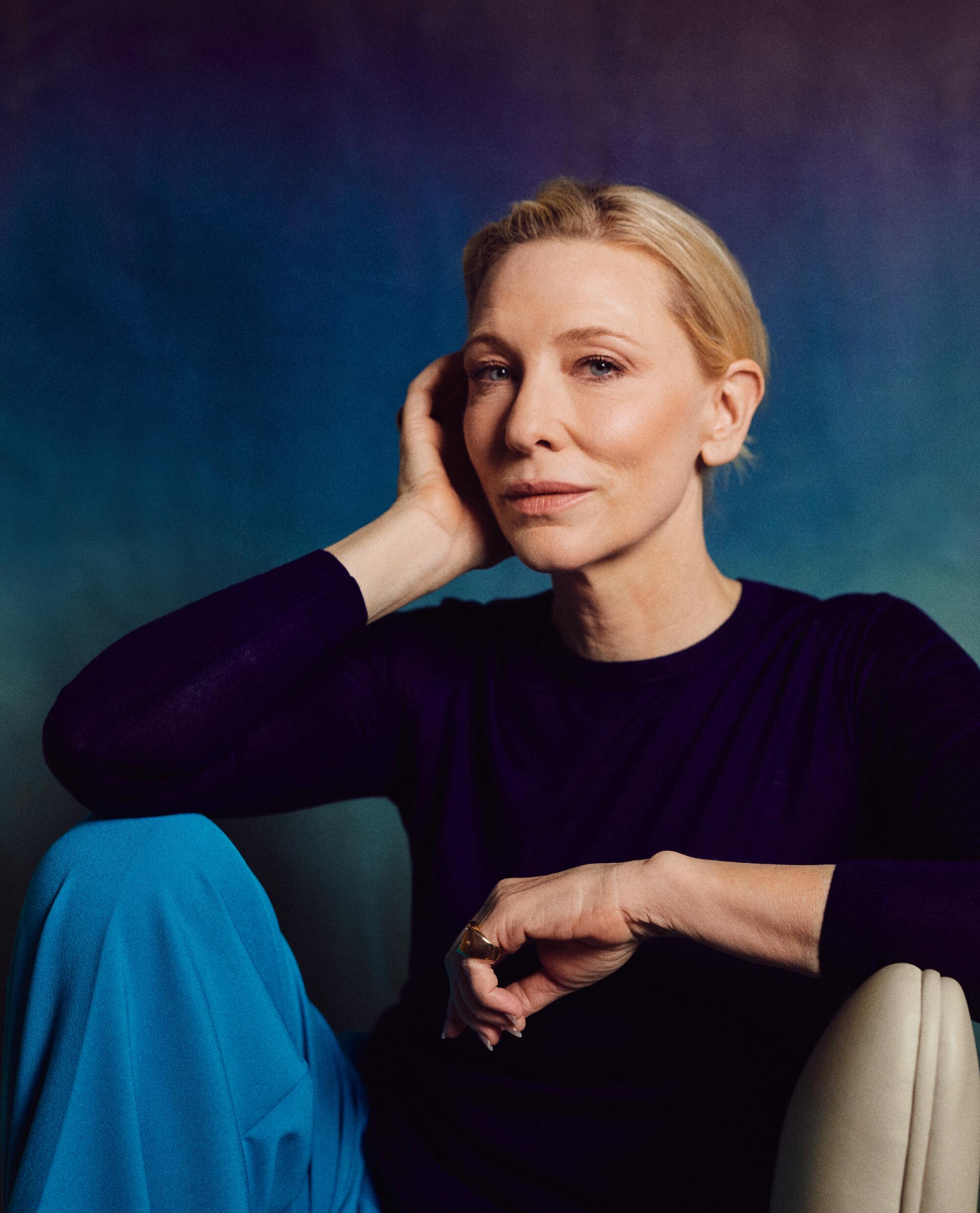 Cate Blanchett sits on a chair, elbow resting on her raised knee.