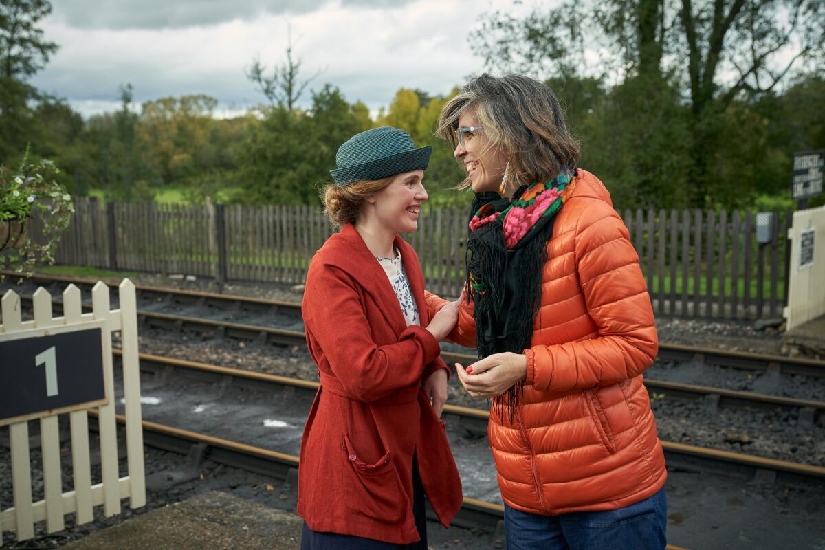 Two women laugh together near a railroad track.