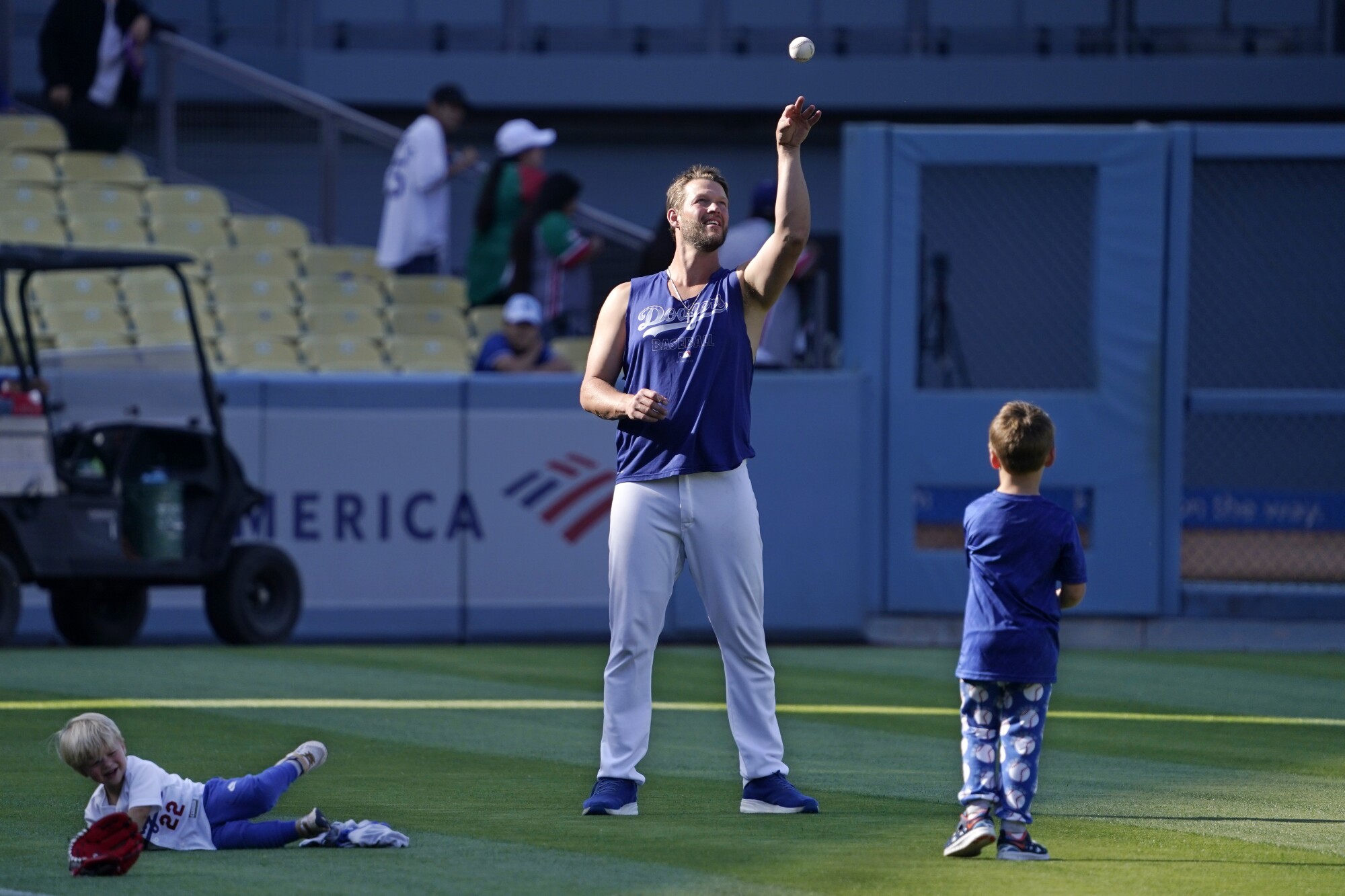 Clayton Kershaw plays catch with his son Charley, right, while his other son Cooper rolls around on the grass.