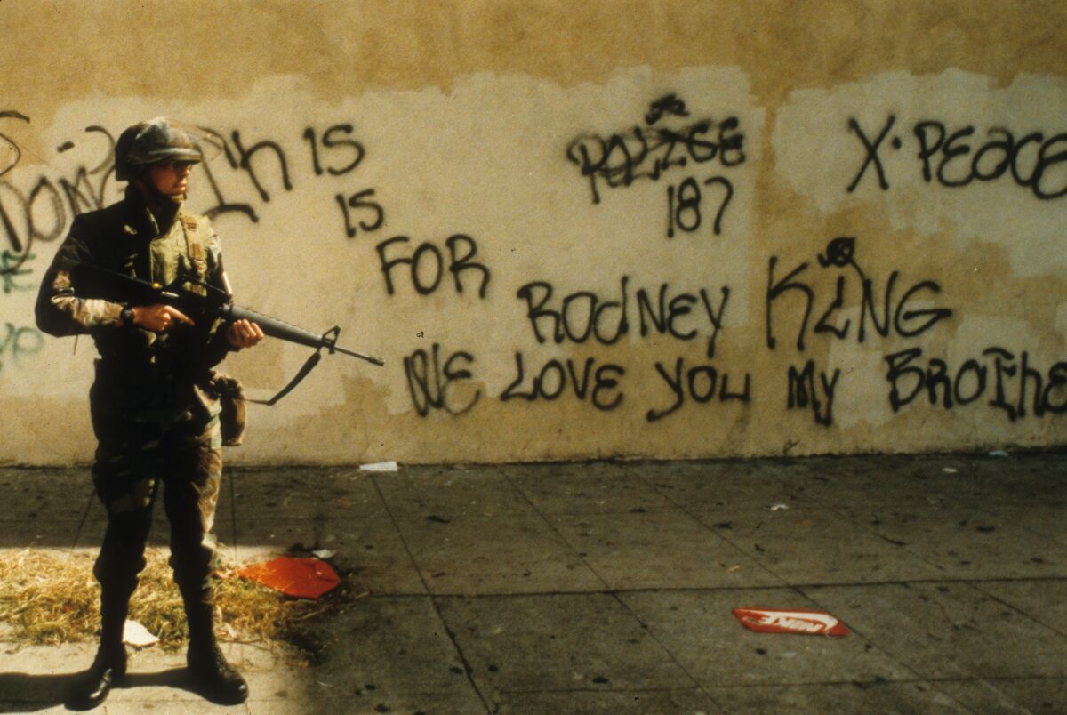 A National Guardsman stands at alert near graffiti that spells out support for Rodney King on April 30, 1992.