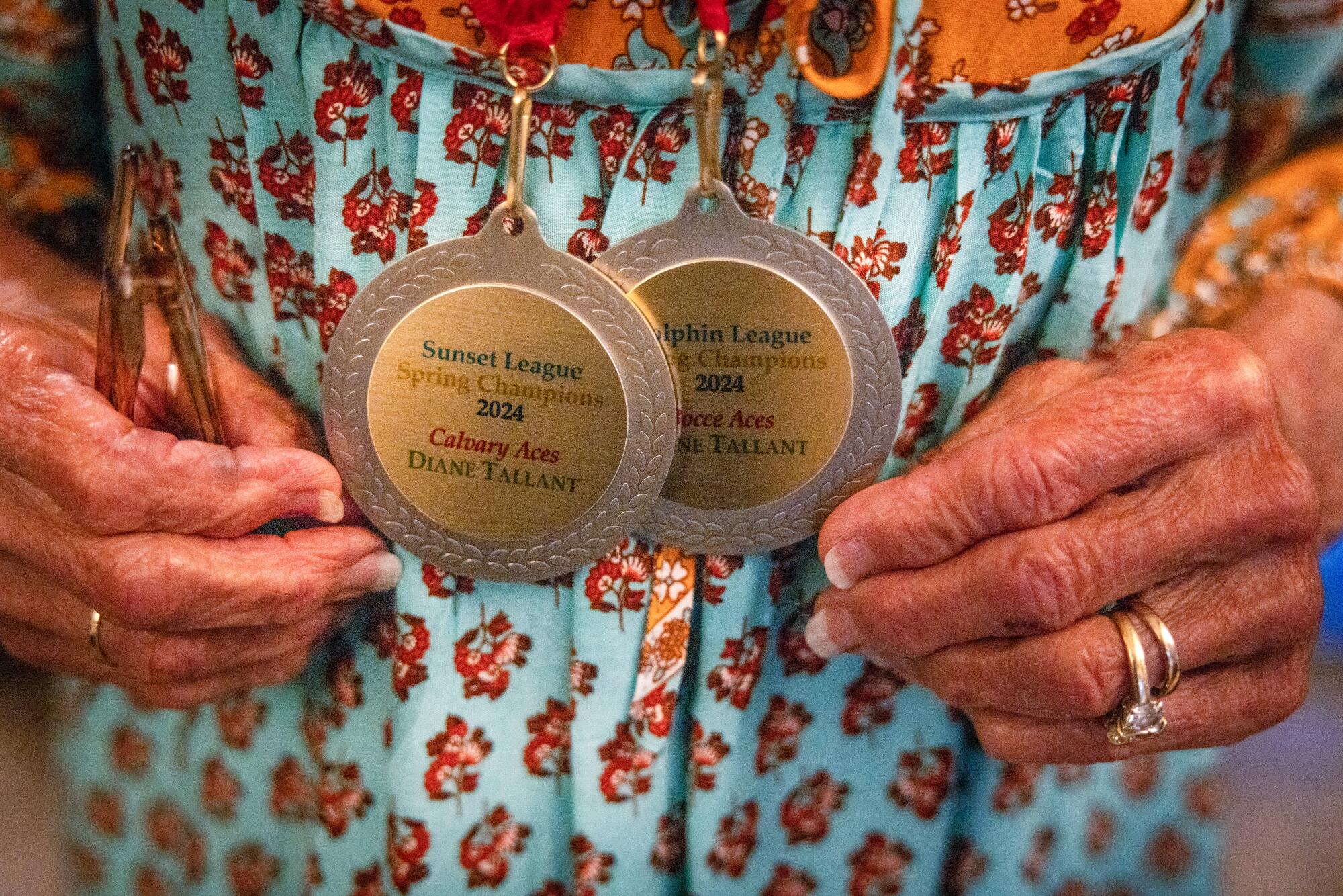 A close-up of a woman's hands holding two medals.