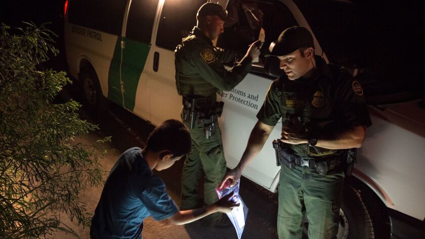 Border Patrol agents Edgar Cano, right, and Richard Schweitzer, left, take shoelaces from unaccompanied minor Darwin, 11, center who crossed the Rio Grande on a raft in Hidalgo, Texas, on March 24, 2017.