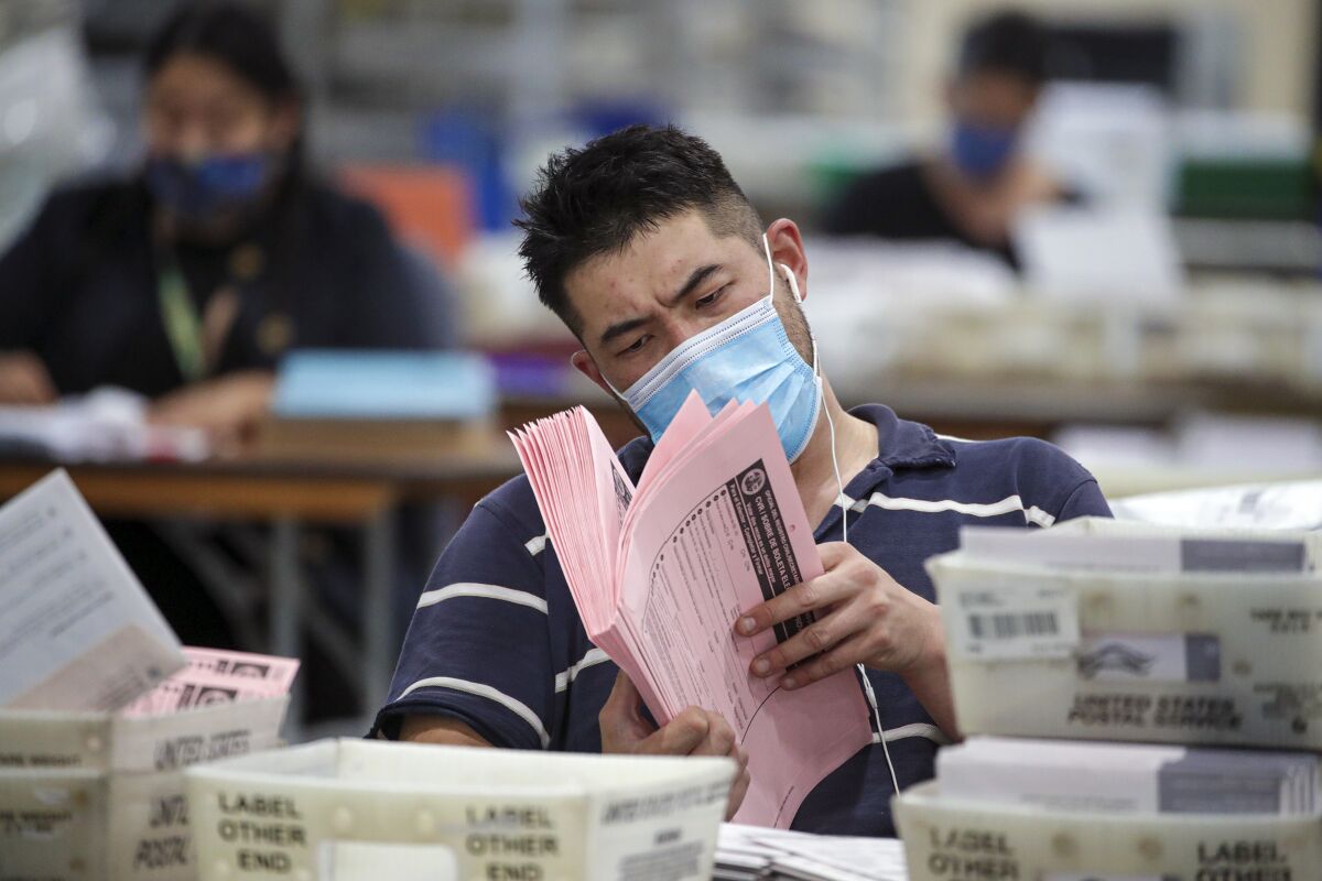 A man in a mask holds and looks closely through a stack of ballots. 