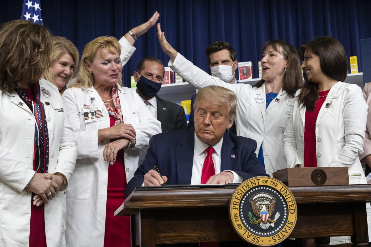 Flanked by supporters in lab coats, President Trump signs executive orders on lowering drug prices, in July 2020.