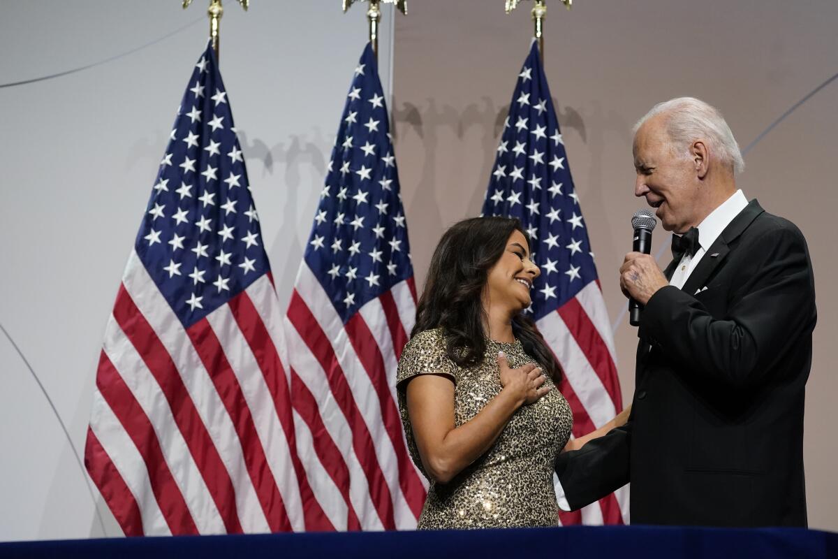 Biden speaks to a woman through a microphone in front of two American flags. 