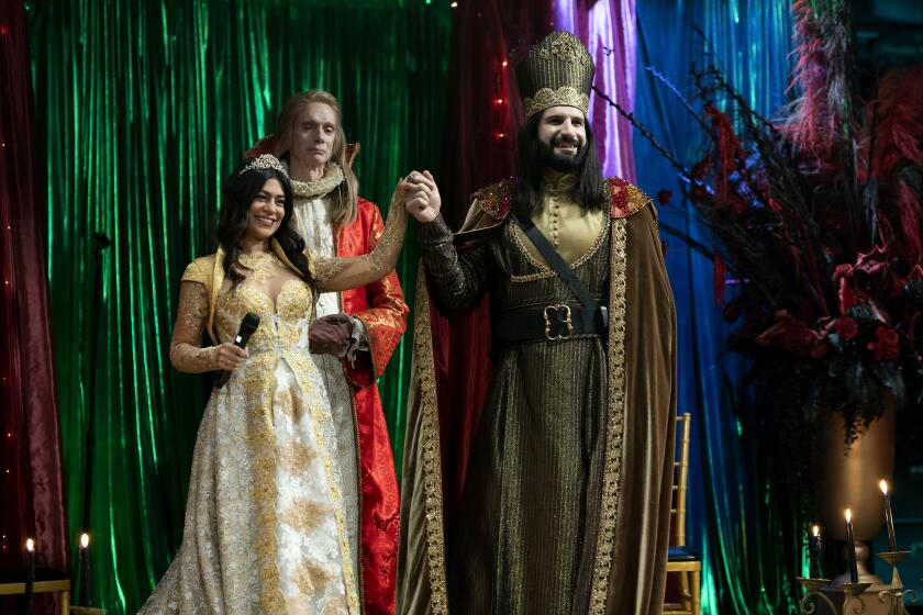 The couple in gold are from the wedding episode. The two feature the bride, Marwa, the officiant in red who is the Baron (Doug Jones) and Nandor, the groom. "WHAT WE DO IN THE SHADOWS" -- "The Wedding" -- Season 4, Episode 6 (Airs August 2) - Pictured: Parisa Fakhri as Marwa, Doug Jones as the Baron, Kayvan Novak as Nandor. CR: Russ Martin: FX