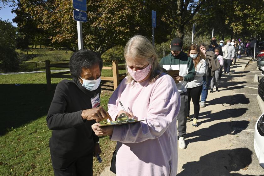 Poll worker Mattie Norman, left, helps Deborah Wood fill out paperwork as Gwinnett County voters wait in lines to cast their ballots for the general election at the Shorty Howell Park Activity Building in Duluth, Ga., on the last day of early voting on Friday, Oct. 30, 2020. (Hyosub Shin/Atlanta Journal-Constitution via AP)