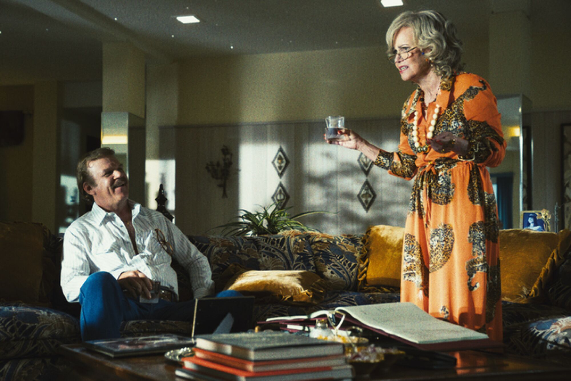A woman in an orange dress holding a cocktail holds forth as a man in a white shirt looks on