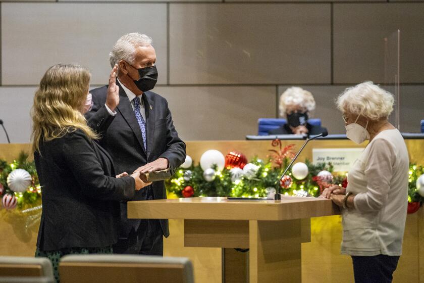 Evelyn Hart, right, administers the oath of office for Brad Avery while his wife Julie Clevenger holds a bible during a swearing in ceremony for Newport Beach City Council Members on Tuesday, December 8.