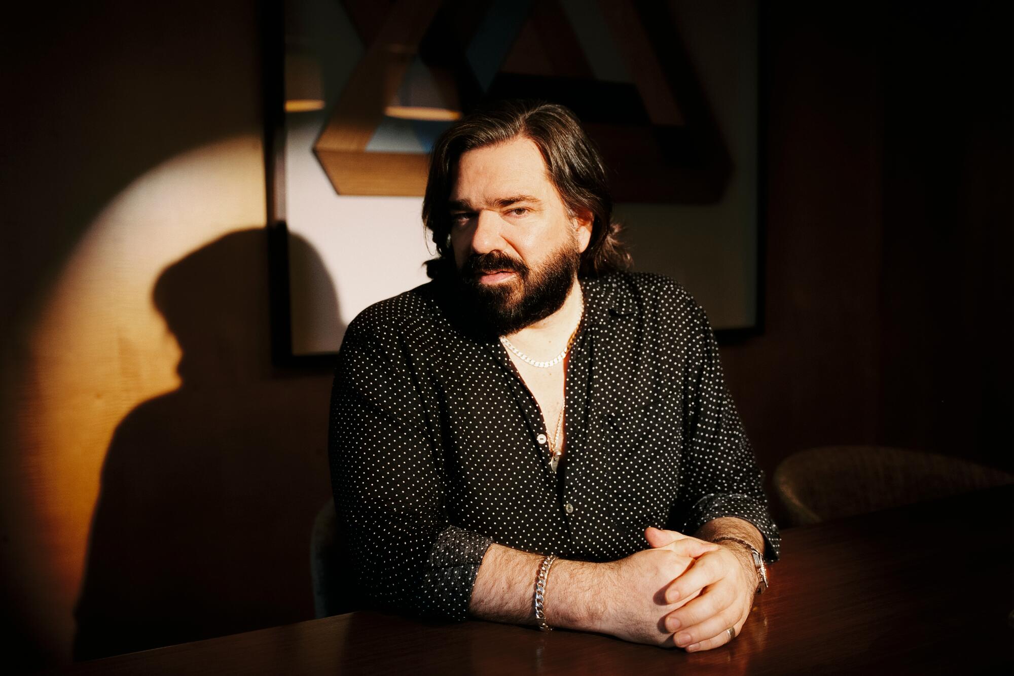 Matt Berry sits in a dark space lighted by a bright spotlight for a portrait.