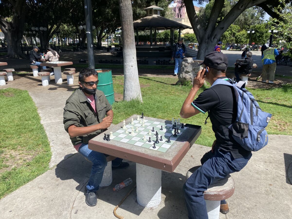 Two men play chess at an outdoor table.