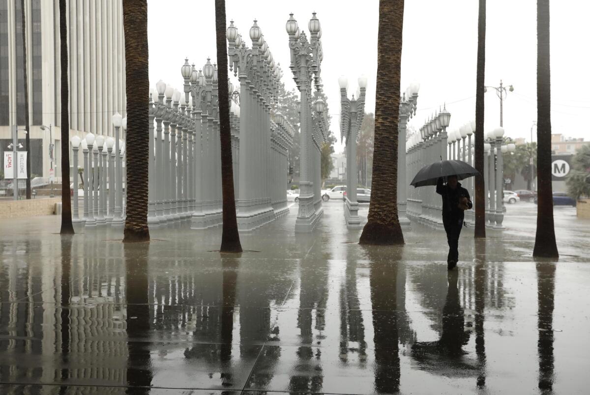 A visitor to the Los Angeles County Museum of Art makes his way through the rain and walks by Chris Burden's sculpture "Urban Light" during an atmospheric river storm in February 2019. The first atmospheric river of 2020 will make its way to L.A. next week.