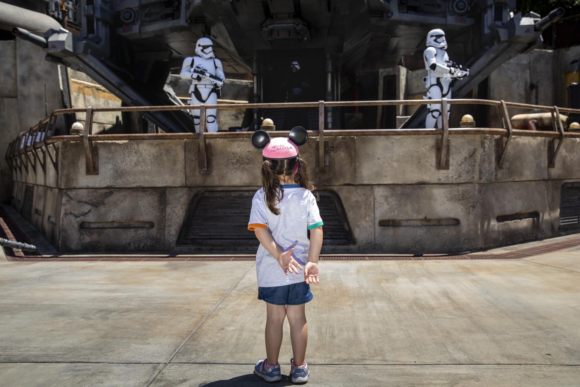 A girl in mouse ears watches two stormtrooper characters behind a railing.