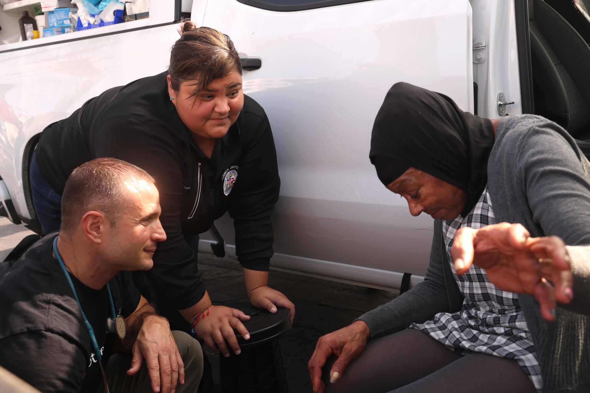 Seorang pria dan seorang wanita berbicara dengan seorang wanita di dekat pintu truk yang terbuka. 