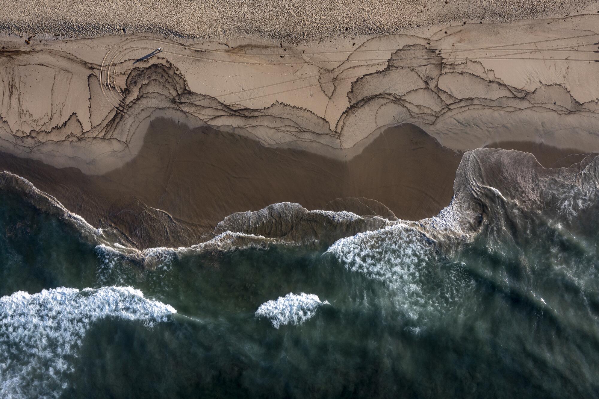 An aerial view of a major oil spill washing ashore with birds feeding at the water's edge on the border of Huntington Beach 