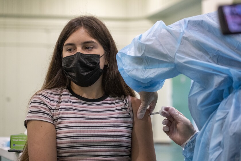 A girl wearing a mask is administered a shot by a healthcare worker