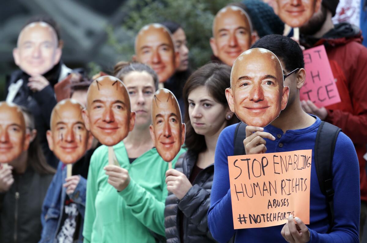 Demonstrators hold images of Amazon CEO Jeff Bezos over their faces.