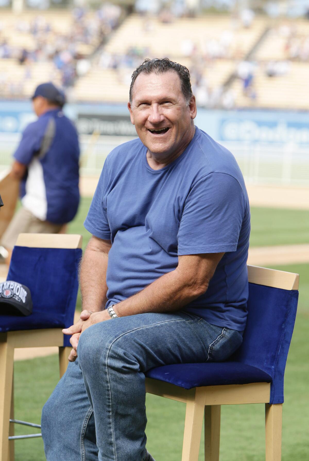 A man sits in a director's chair in a blue T-shirt.