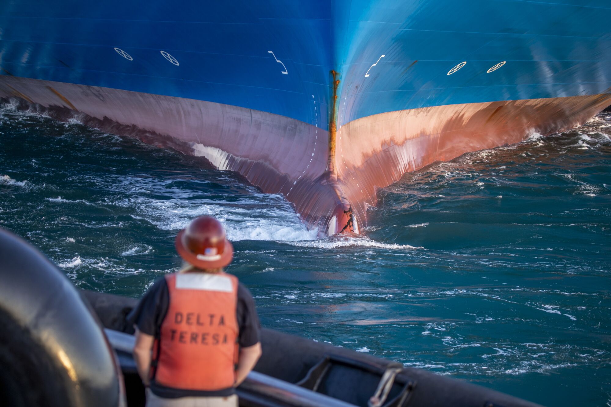The bow of a container ship approaches the tugboat Delta Teresa as deckhand Jessica Huber watches.