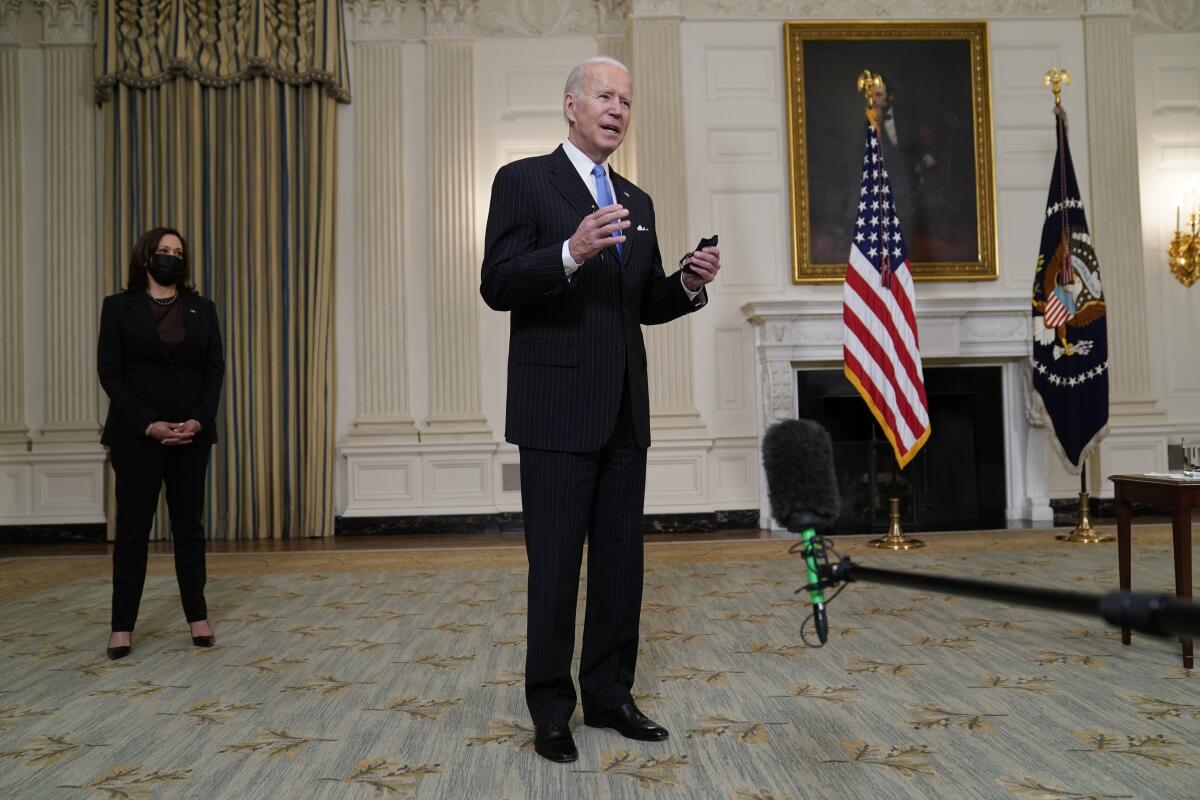 President Joe Biden holds a face mask after speaking about efforts to combat COVID-19, in the State Dining Room of the White House, Tuesday, March 2, 2021, in Washington. Vice President Kamala Harris is at left. (AP Photo/Evan Vucci)