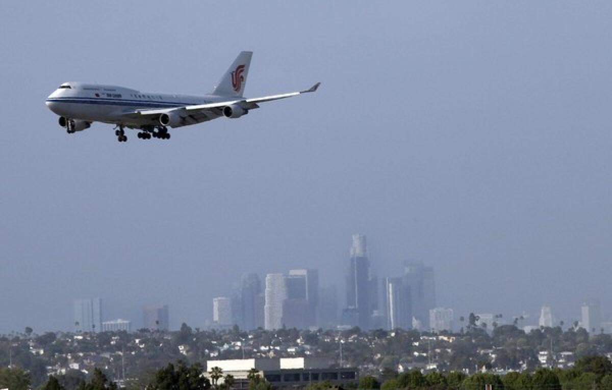 A plane approaches LAX for a landing with downtown Los Angeles in the background.