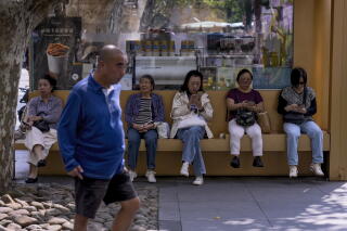 A man walks by as women rest on a bench in front of a cafe near a public park in