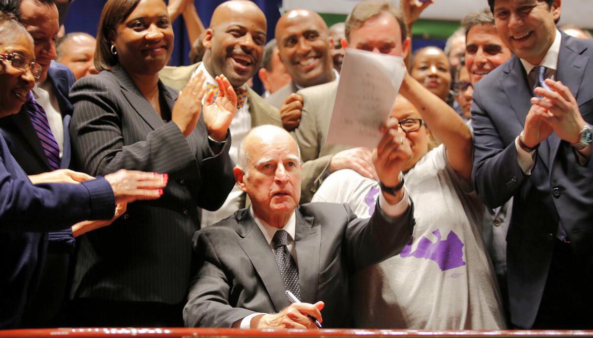 California Gov. Jerry Brown holds a signed copy of the minimum wage bill, which will raise the wage to $15 an hour by 2022.