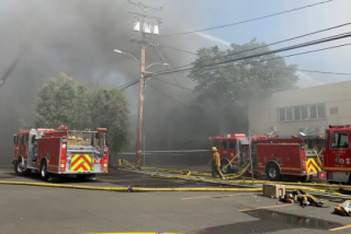 Four fire trucks sit amid thick smoke on a city street.