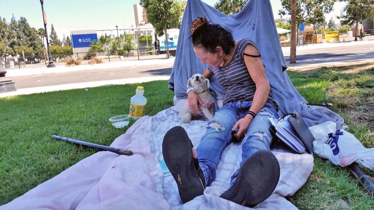 Jewel Lopez, 52, and her dog, Missy, spend some days under a shady tree near the El Cajon Police Station.