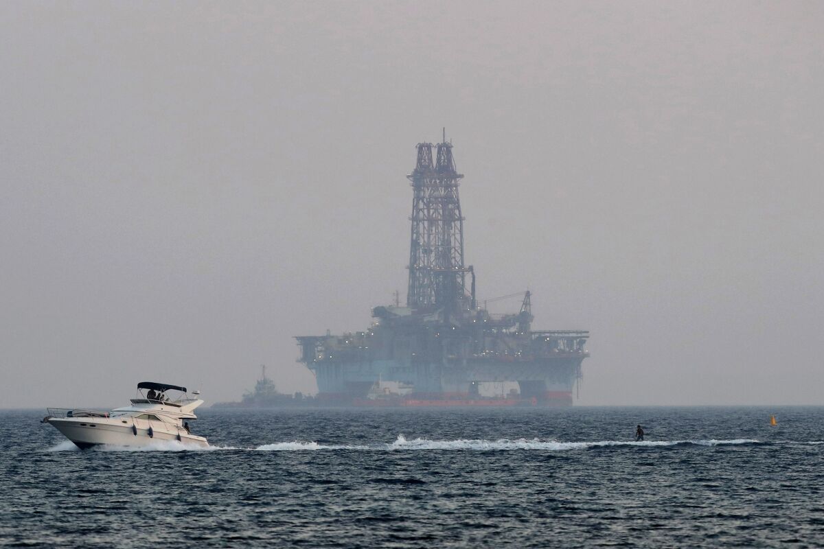 FILE - In this Sunday, July 5, 2020, file photo, an offshore drilling rig is seen in the waters off Cyprus' coastal city of Limassol as a boat passes with a skier. A climate change conference will underscore to policymakers in the Middle East and the east Mediterranean that the switch from fossil fuels to renewable energy sources is needed urgently because greenhouse gas emissions are helping to drive up regional temperatures faster than in many other inhabited parts of the world. (AP Photo/Petros Karadjias, File)