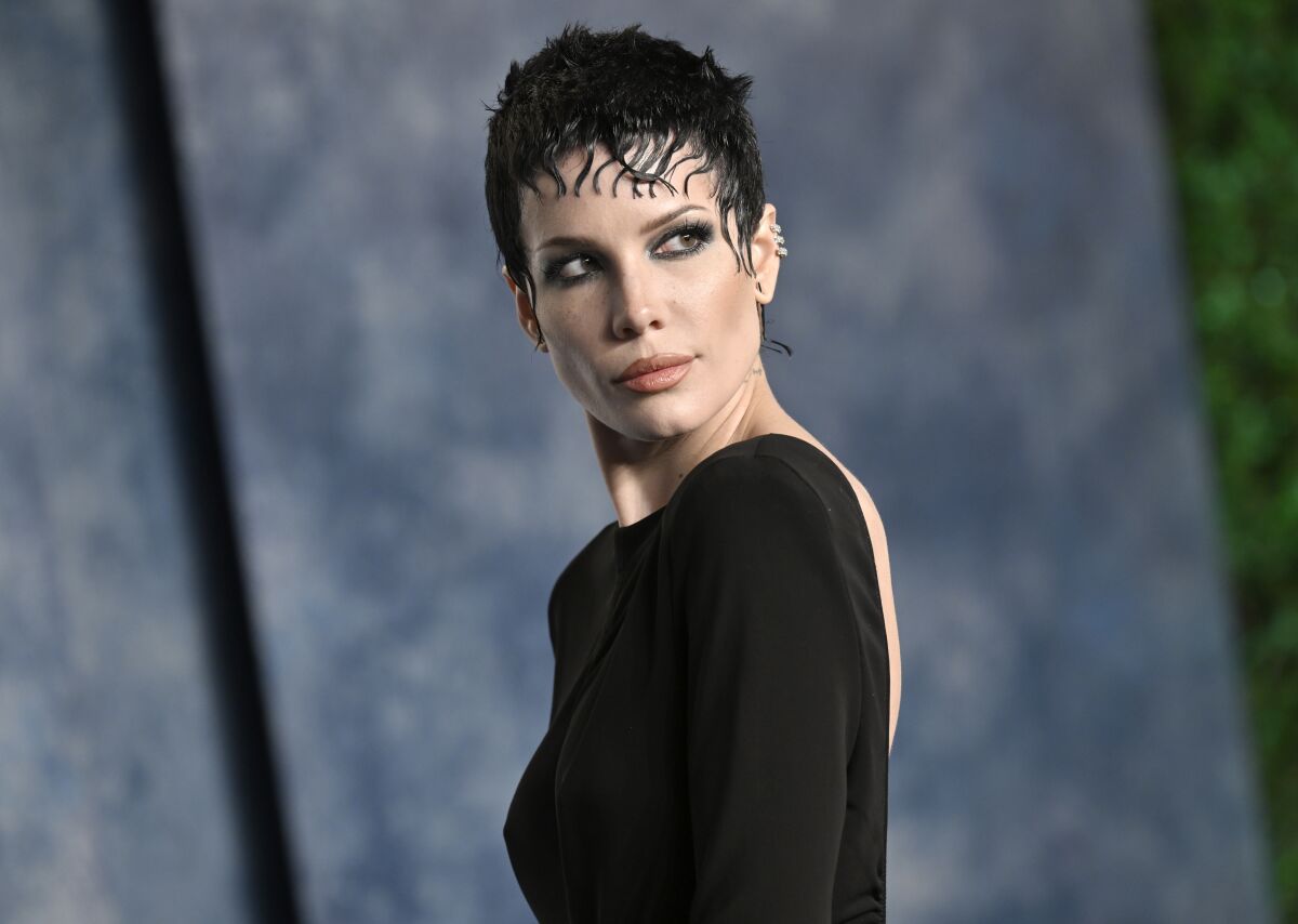 Halsey with dark hair and dark eye makeup posing in a backless dress.
