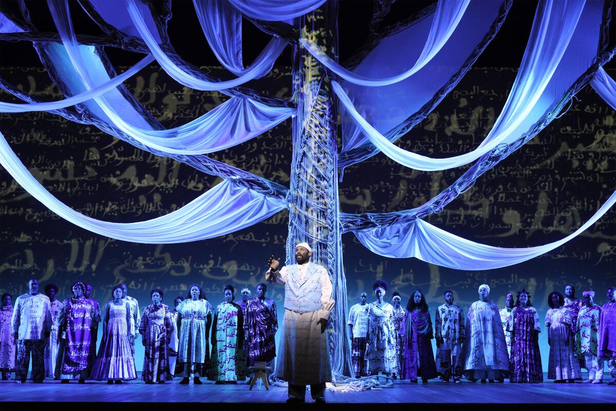 Opera singer Jamez McCorkle performs in costume covered in script on a stage illuminated with blue light in "Omar"