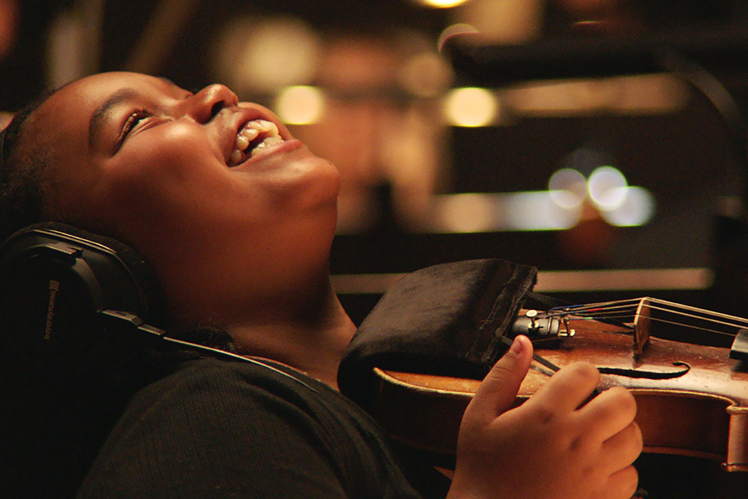 A youngster holding a violin laughs happily in "The Last Repair Shop."