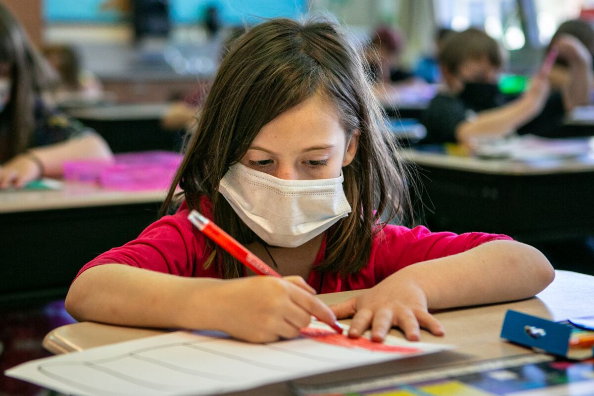 An elementary schoolchild at her desk wearing a mask