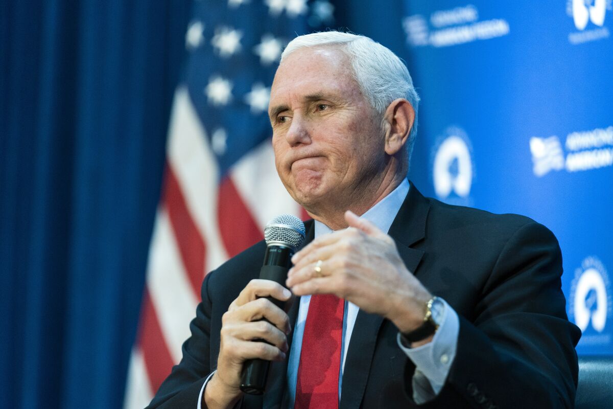 Former Vice President Mike Pence holds a microphone and gestures while speaking