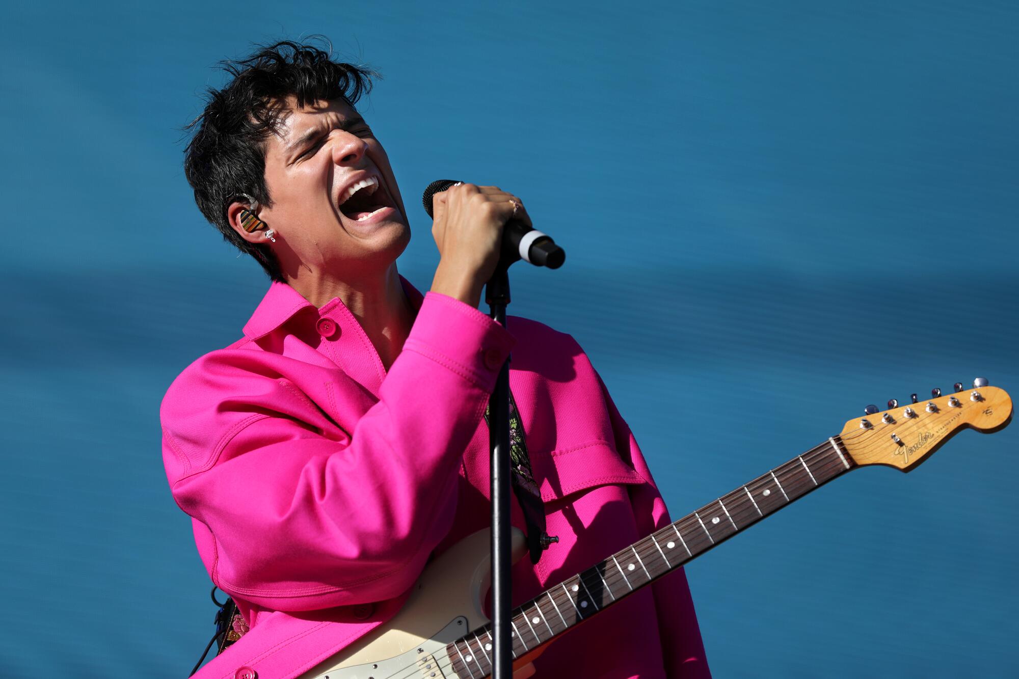 Omar Apollo performs wearing a bright pink shirt.
