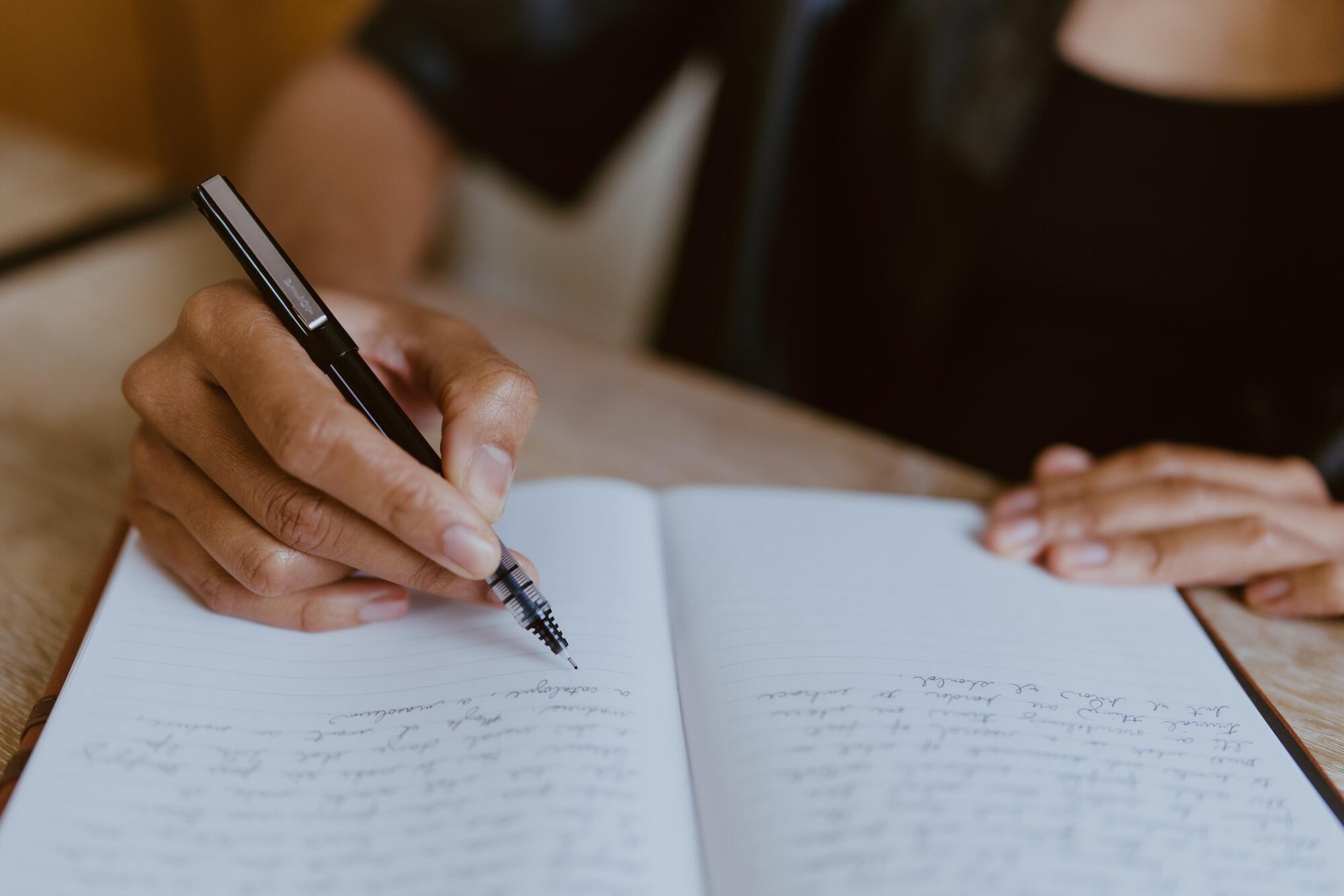 A close-up of a Black woman's hands shows her writing in a notebook.