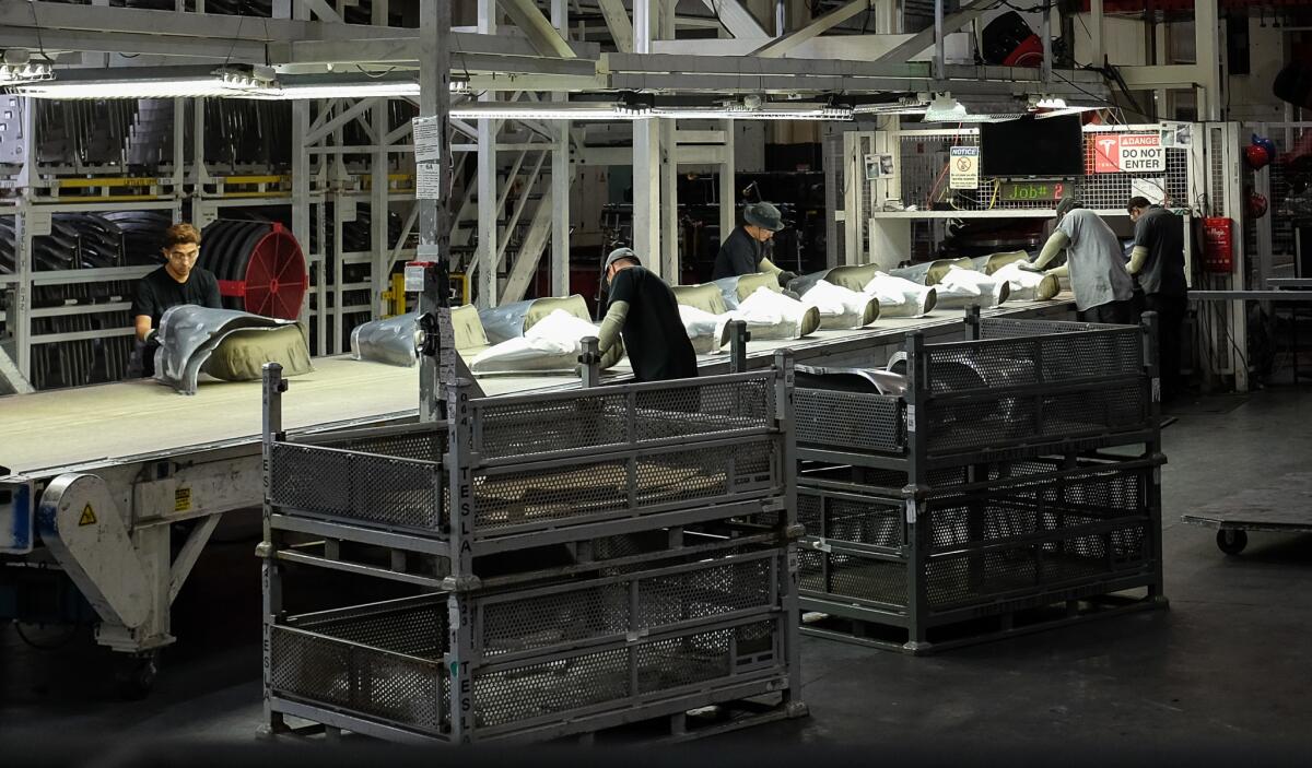 Workers at a stamping machine at Tesla's electric car factory in Fremont, Calif.