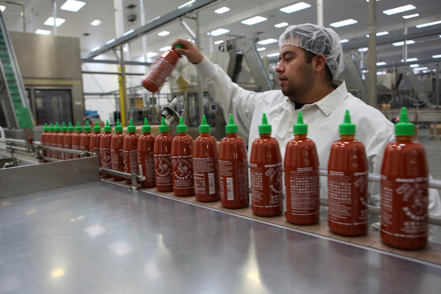 A worker keeps an eye on the production line as freshly filled Sriracha sauce bottles move on a conveyor for packaging at Huy Fong Foods in Irwindale.