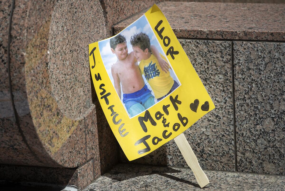 A yellow handmade sign with a photo of two children says "Justice for Mark and Jacob."
