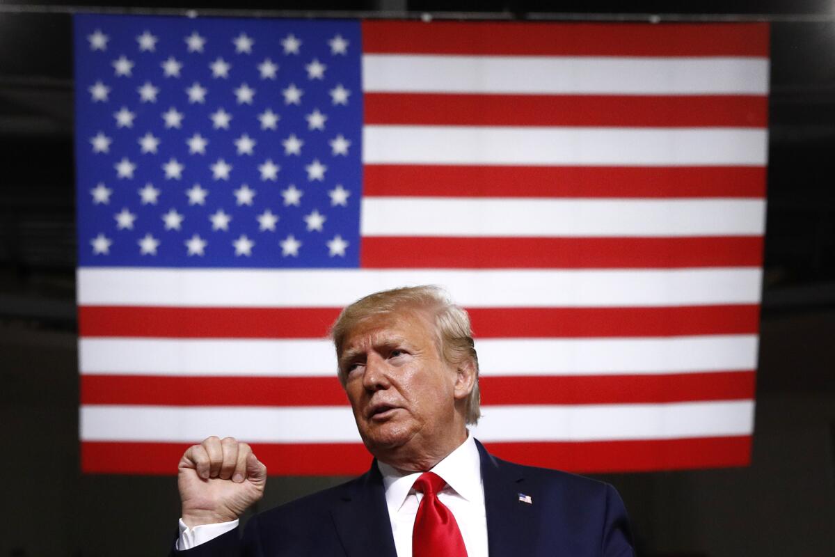 President Trump, right fist lifted, stands in front of an American flag.