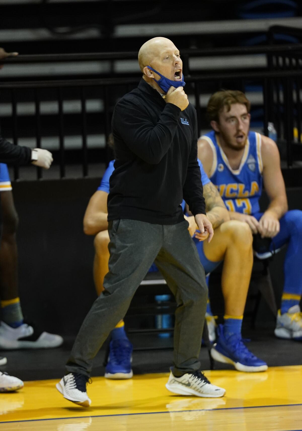 UCLA coach Mick Cronin, on the sideline, pulls down his face mask as he shouts.