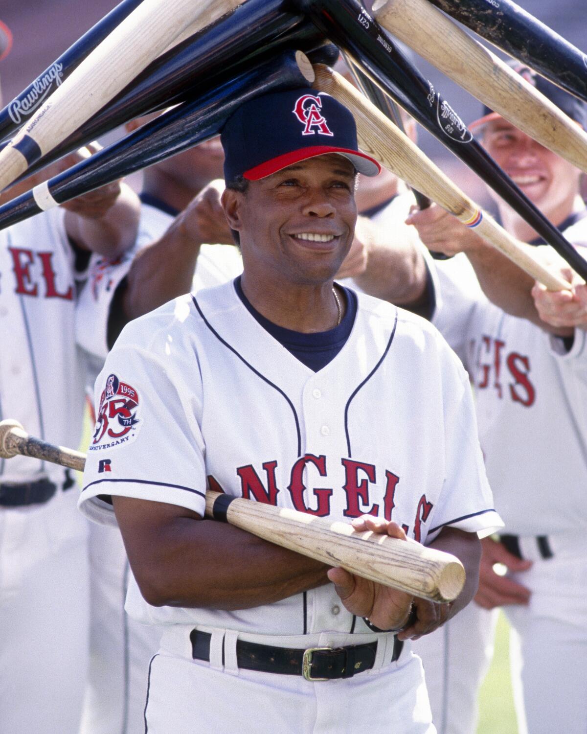 Angels hitting coach Rod Carew is surrounded by bats and poses for photographs before a game in May 1995.