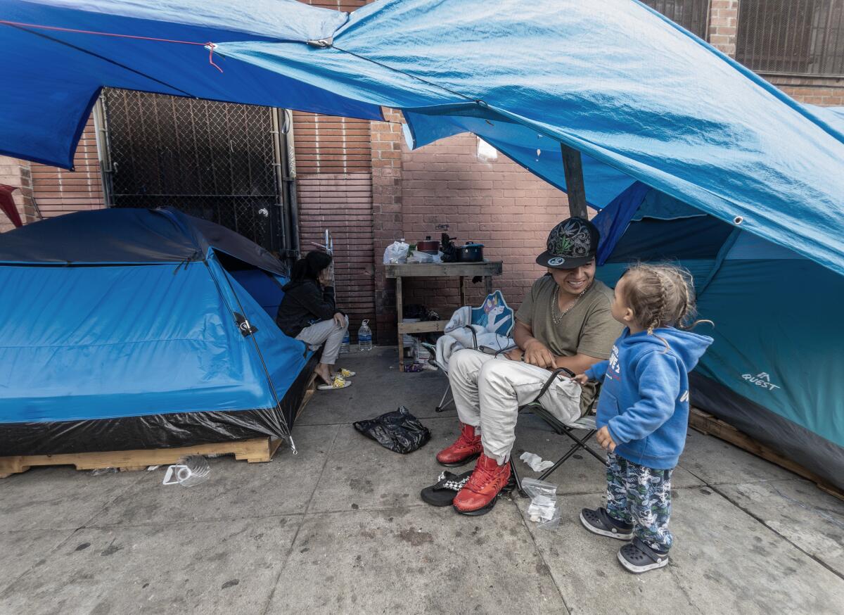 An adult and a child under a tarp on a sidealk.