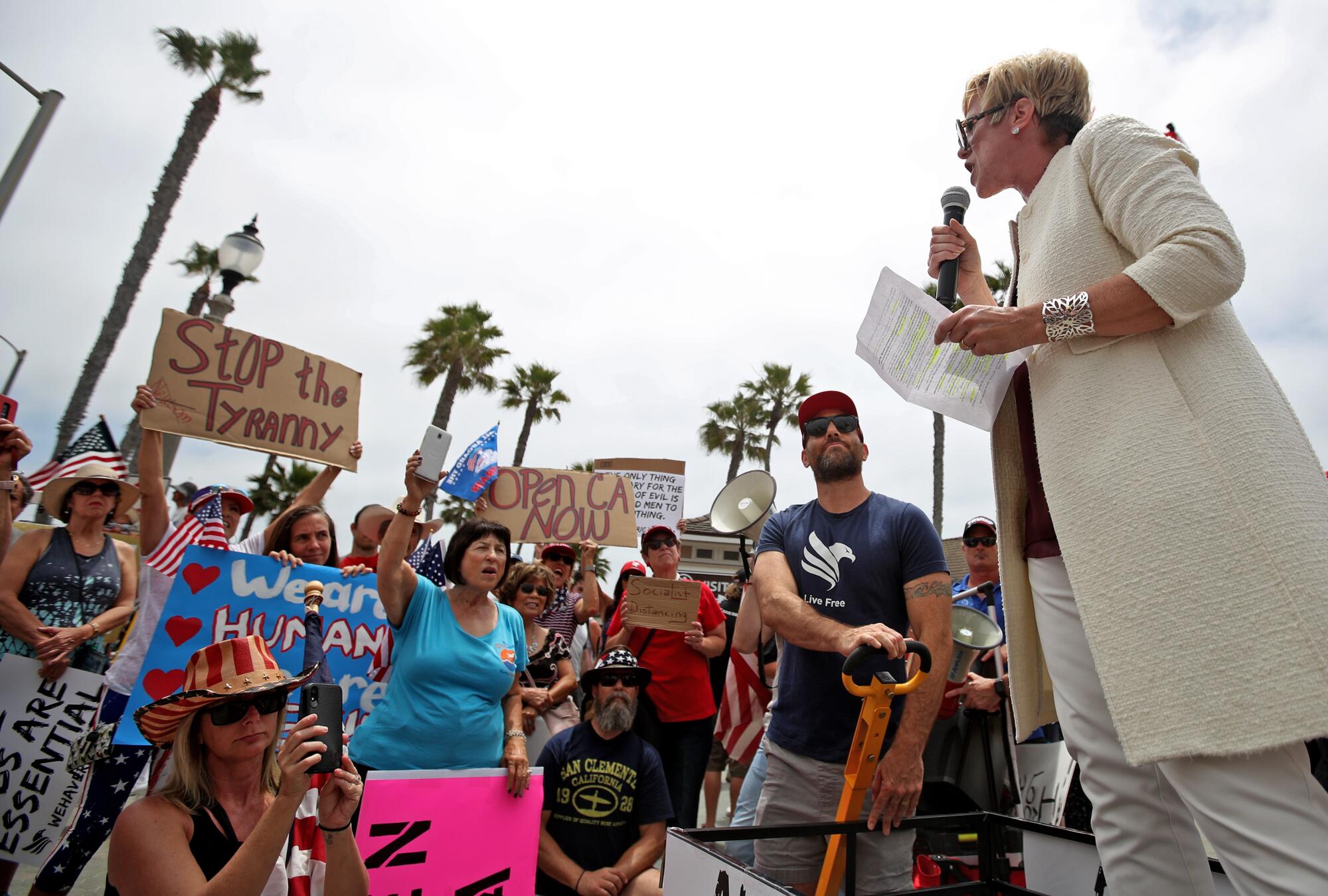 Leigh Dundas peaks at a protest to a group of people with signs 