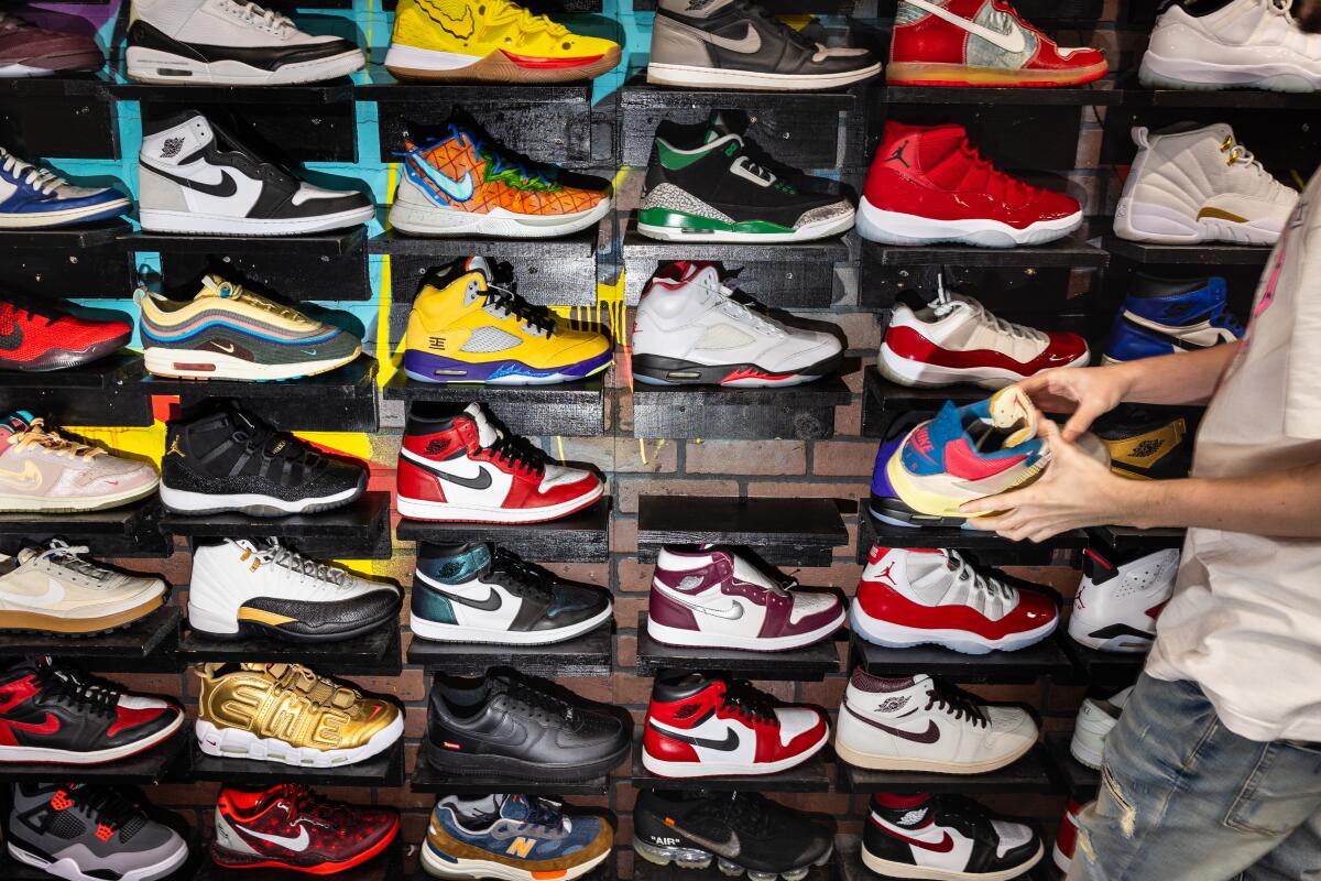 A man stands beside a wall of sneakers while holding a sneaker in his hands