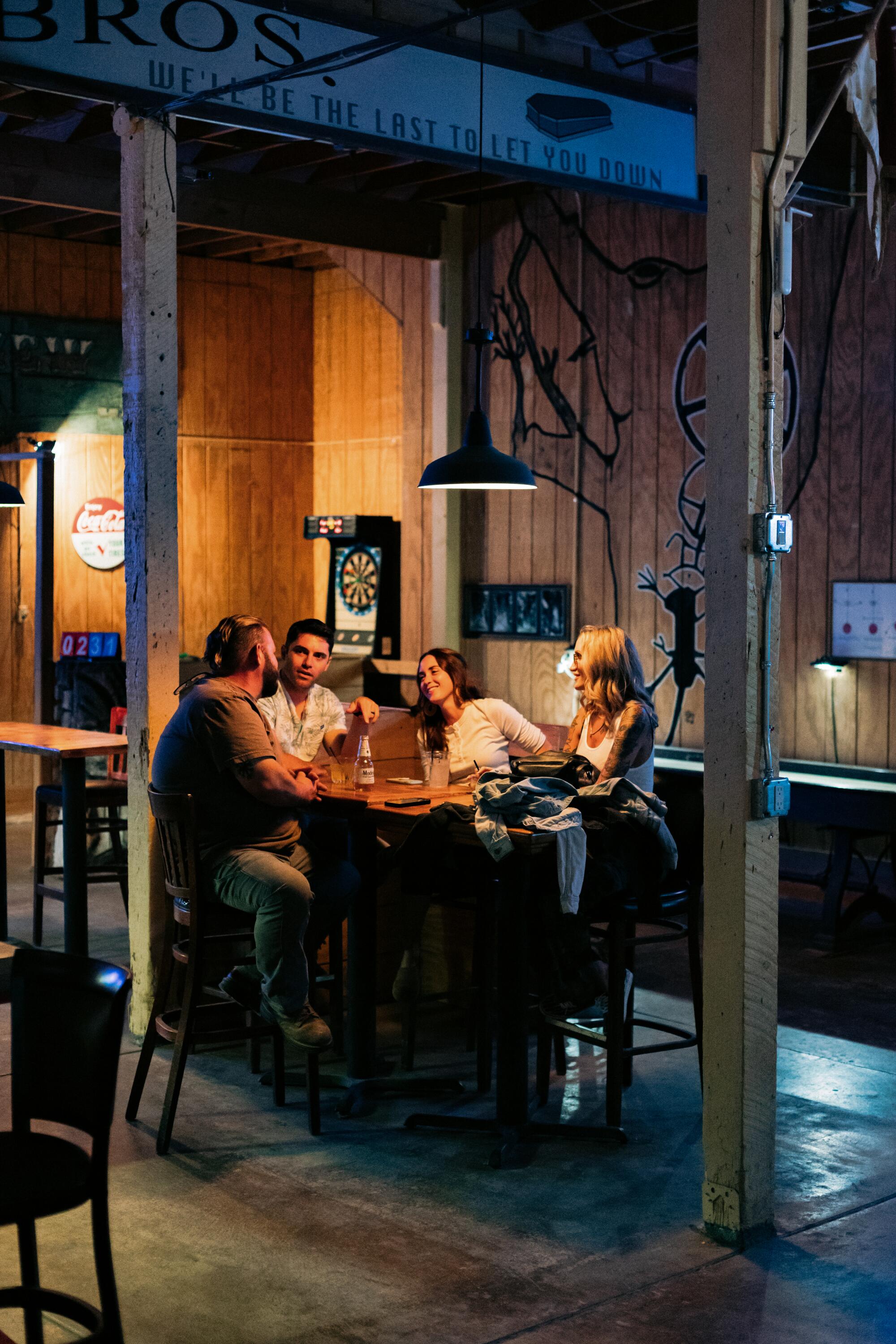 A group of people sit around a hightop table at a bar.