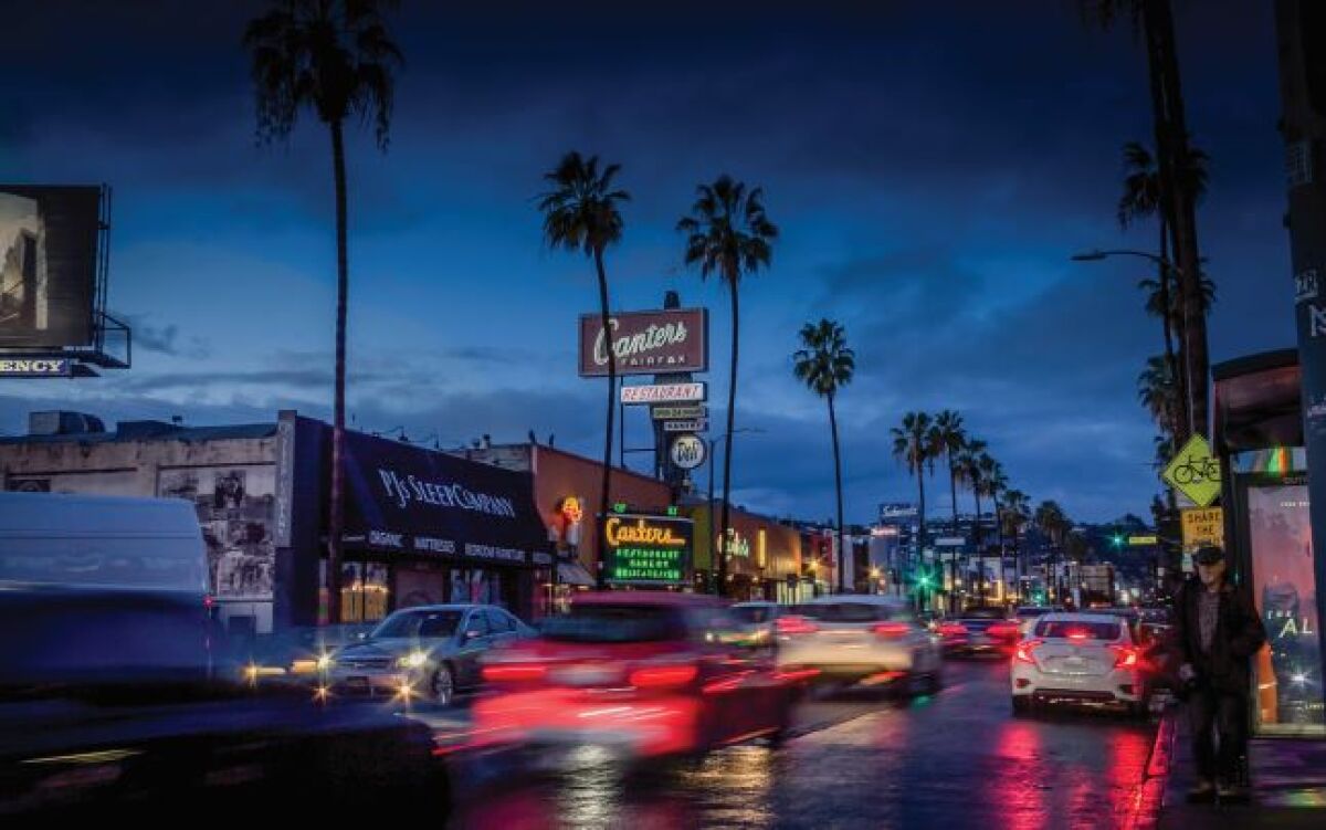 A nighttime photo of Canter’s Deli with cars passing by on Fairfax Avenue in Los Angeles.